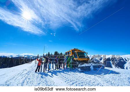 Stock Image - Group portrait of male and female skiers on ski slope by snow coach, Aspen, Colorado, USA. Fotosearch