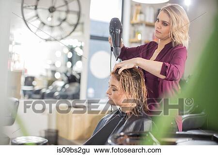 Hairdresser blow drying customer's hair in salon View Large Photo Image Stock Photograph - Hairdresser blow drying customer's hair in salon. Fotosearch