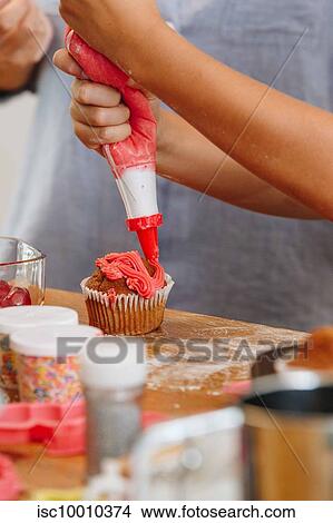 Hand decorating cupcake with red coloured frosting View Large Photo Image Picture - Hand decorating cupcake with red coloured frosting. Fotosearch