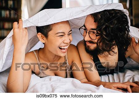 Stock Photography - Happy couple under covers in bed. Fotosearch