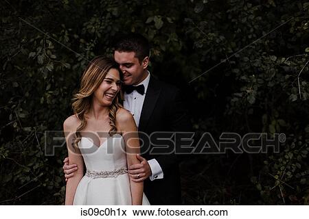 Stock Photo - Happy young bride and groom laughing in front of foliage. Fotosearch