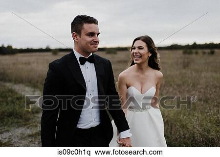 Happy young couple strolling hand in hand through field on wedding day View Large Photo Image Stock Photography - Happy young couple strolling hand in hand through field on wedding day. Fotosearch