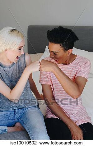 Stock Image - Happy young woman and boyfriend fist bumping each other on bed. Fotosearch