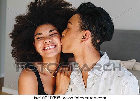Happy young woman being kissed on cheek by boyfriend in bedroom, head and shoulders View Large Photo Image Stock Photo - Happy young woman being kissed on cheek by boyfriend in bedroom, head and shoulders. Fotosearch
