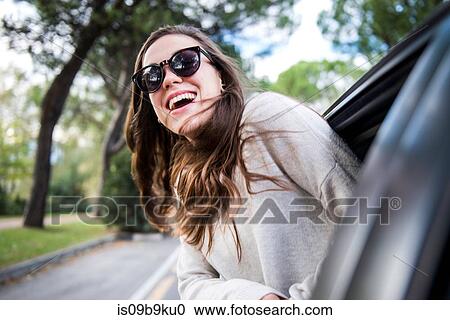 Happy young woman on road trip leaning out of car window View Large Photo Image Stock Image - Happy young woman on road trip leaning out of car window. Fotosearch