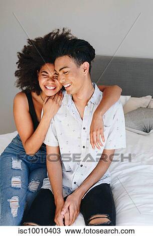 Happy young woman with arms around boyfriend while sitting on bed View Large Photo Image Stock Image - Happy young woman with arms around boyfriend while sitting on bed. Fotosearch