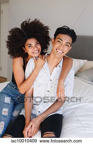 Happy young woman with arms around boyfriend while sitting on bed, portrait View Large Photo Image Stock Photo - Happy young woman with arms around boyfriend while sitting on bed, portrait. Fotosearch