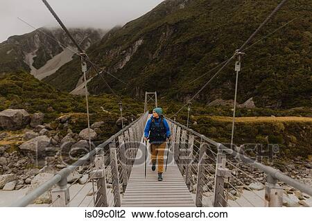 Stock Image - Hiker crossing suspension bridge, Wanaka, Taranaki, New Zealand. Fotosearch
