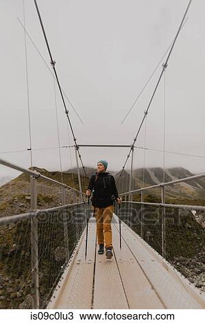 Stock Image - Hiker crossing suspension bridge, Wanaka, Taranaki, New Zealand. Fotosearch