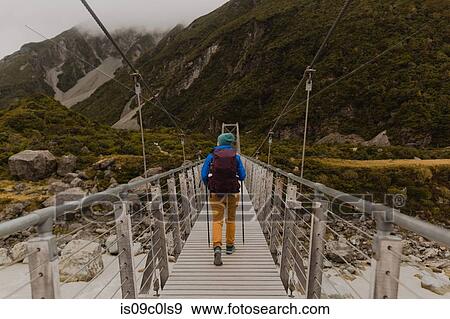 Stock Photo - Hiker crossing suspension bridge, Wanaka, Taranaki, New Zealand. Fotosearch