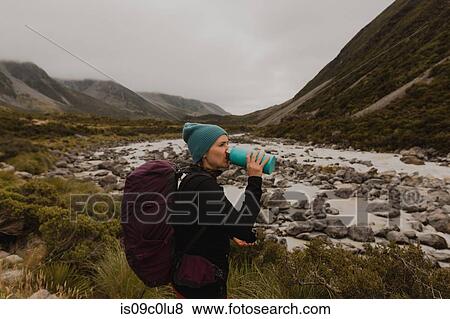 Stock Photo - Hiker drinking, enjoying view of wilderness, Wanaka, Taranaki, New Zealand. Fotosearch