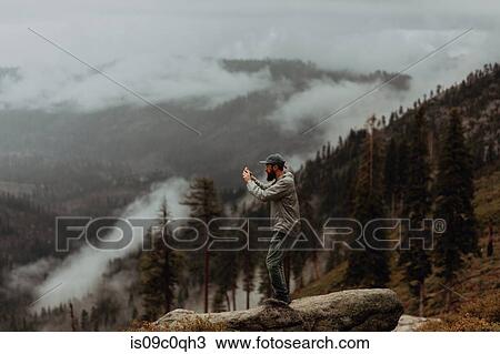 Stock Image - Hiker taking photograph of view of fog covering valley, Yosemite National Park, California, United States. Fotosearch