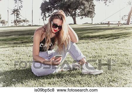 Stock Photo - Hip young woman using mobile phone in park. Fotosearch