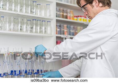 Picture - Lab worker taking dye from beaker using long pipette. Fotosearch