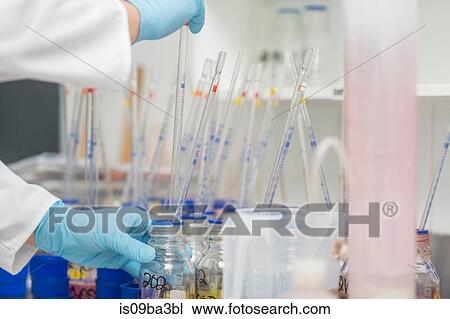 Stock Image - Lab worker taking dye from beaker using long pipette. Fotosearch