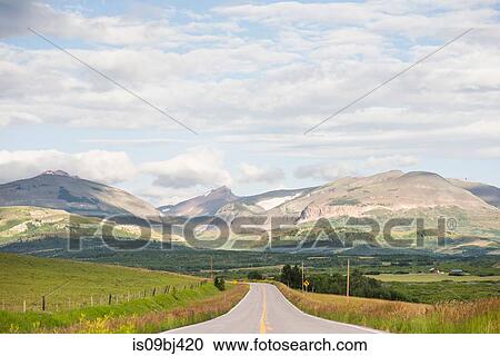 Stock Image - Landscape with rural road through mountain valley, Browning, Montana, USA. Fotosearch