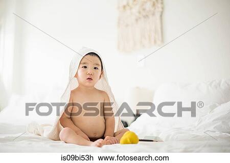 Stock Image - Little boy with hooded towel in bed. Fotosearch