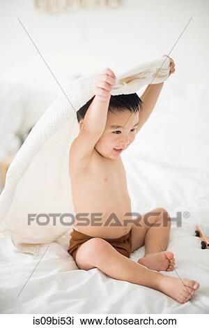 Stock Image - Little boy with hooded towel in bed. Fotosearch