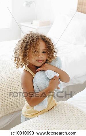 Stock Image - Little girl cuddling soft toy in bedroom. Fotosearch