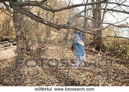 Stock Image - Little girl swinging on tree branch in forest. Fotosearch