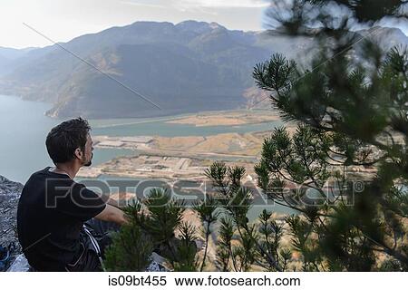 Stock Photography - Male rock climber looking out over lake from The Chief, Squamish, British Columbia, Canada. Fotosearch