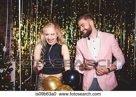 Stock Image - Man and woman at party, holding drinks, laughing. Fotosearch