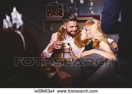 Picture - Man and woman at party, sitting on sofa, holding drinks, making a toast. Fotosearch