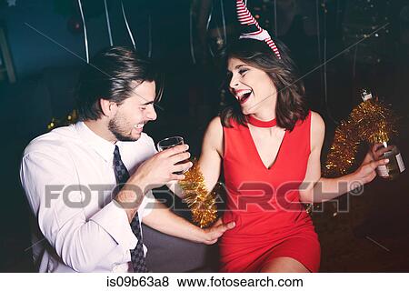 Stock Photo - Man and woman sitting together at party, holding drinks, laughing. Fotosearch