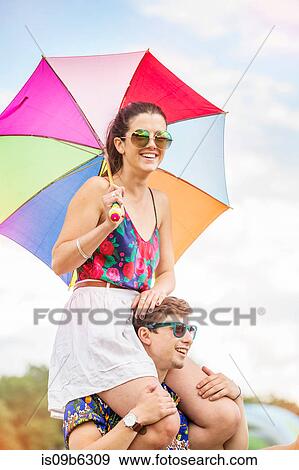 Stock Photo - Man carrying woman holding umbrella on shoulders. Fotosearch