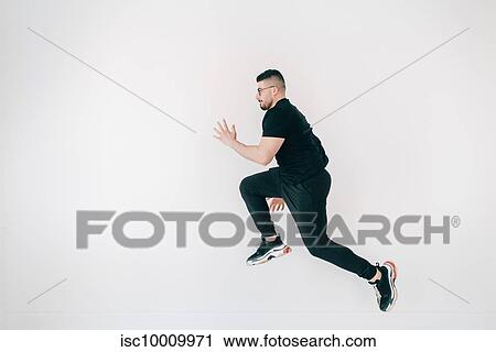 Stock Image - Man doing high jump against white wall. Fotosearch