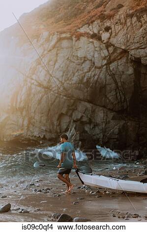 Picture - Man dragging kayak into sea, Big Sur, California, United States. Fotosearch