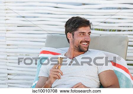 Man enjoying ice cream cone on deckchair View Large Photo Image Stock Photo - Man enjoying ice cream cone on deckchair. Fotosearch