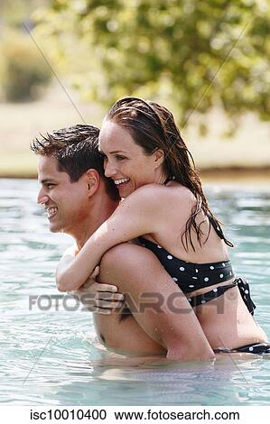 Stock Image - Man giving woman piggyback ride in swimming pool. Fotosearch