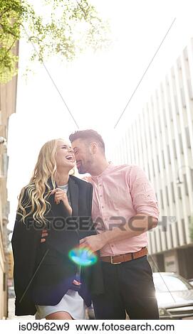 Stock Photo - Man in street sharing suit jacket with woman. Fotosearch
