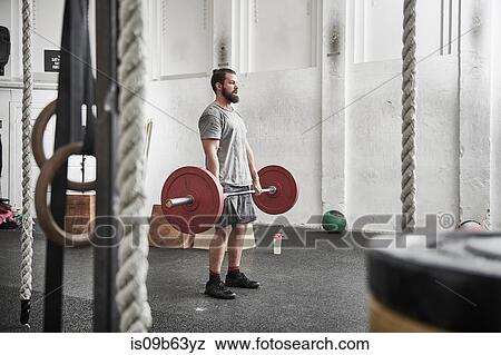 Stock Photo - Man lifting barbell in cross training gym. Fotosearch