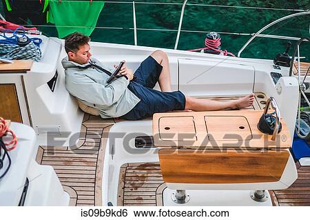 Stock Photograph - Man relaxing aboard yacht looking at digital tablet, Croatia. Fotosearch