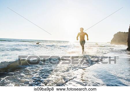 Stock Photo - Man running on El Matador Beach, Malibu, USA. Fotosearch