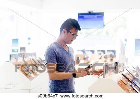 Stock Photo - Man shopping in technology shop looking at smartphone. Fotosearch