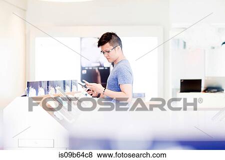 Stock Photo - Man shopping in technology shop looking at smartphone. Fotosearch