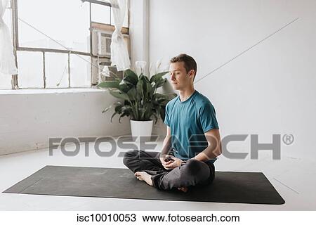Stock Image - Man sitting in lotus pose in yoga studio. Fotosearch