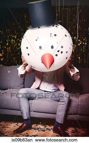 Man sitting on sofa at party, holding snowman head in front of face View Large Photo Image Picture - Man sitting on sofa at party, holding snowman head in front of face. Fotosearch