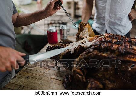 Picture - Man slicing hog roast on table, cropped. Fotosearch