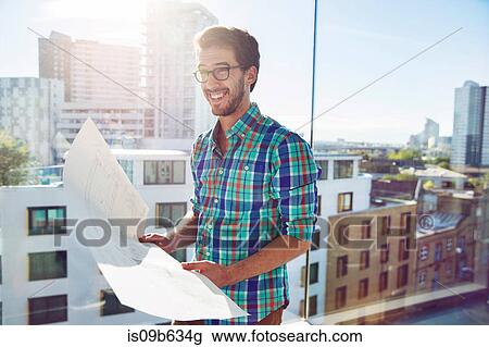 Man, standing beside office window, looking at plans, smiling View Large Photo Image Stock Image - Man, standing beside office window, looking at plans, smiling. Fotosearch
