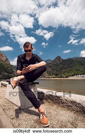Stock Image - Man using mobile phone by beach, Draja, Vaslui, Romania. Fotosearch