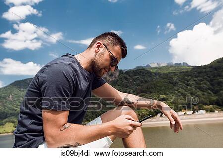 Stock Image - Man using mobile phone by beach, Draja, Vaslui, Romania. Fotosearch