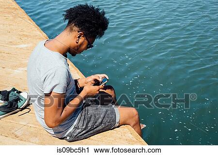 Stock Image - Man using mobile phone by edge of water. Fotosearch