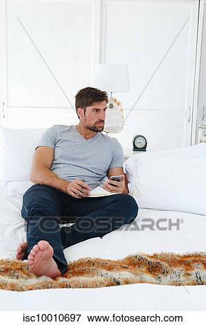 Man using smartphone and writing notes on sofa View Large Photo Image Stock Photo - Man using smartphone and writing notes on sofa. Fotosearch
