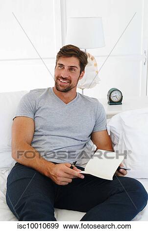 Stock Photo - Man using smartphone and writing notes on sofa. Fotosearch