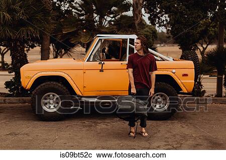 Stock Image - Man with luggage standing by four wheel drive vehicle. Fotosearch
