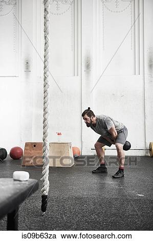 Stock Image - Man working out with kettlebell in cross training gym. Fotosearch